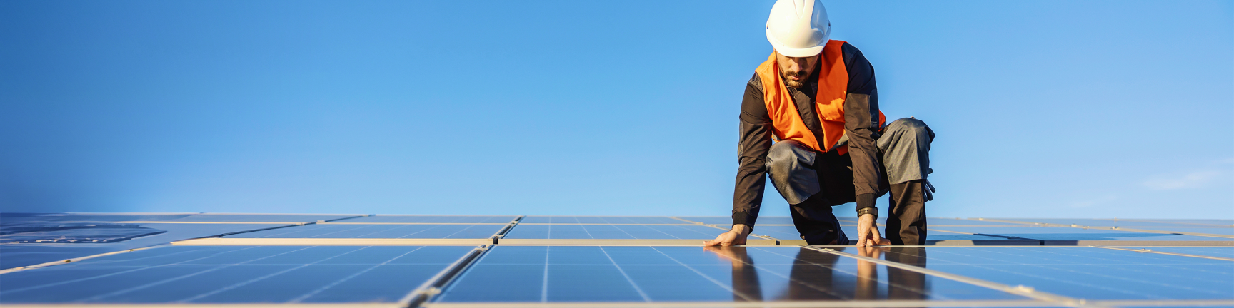 Homme portant un casque accroupi sur des panneaux solaires