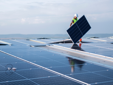 Employé portant un casque en train d'installer un panneau solaire sur le toit d'un bâtiment